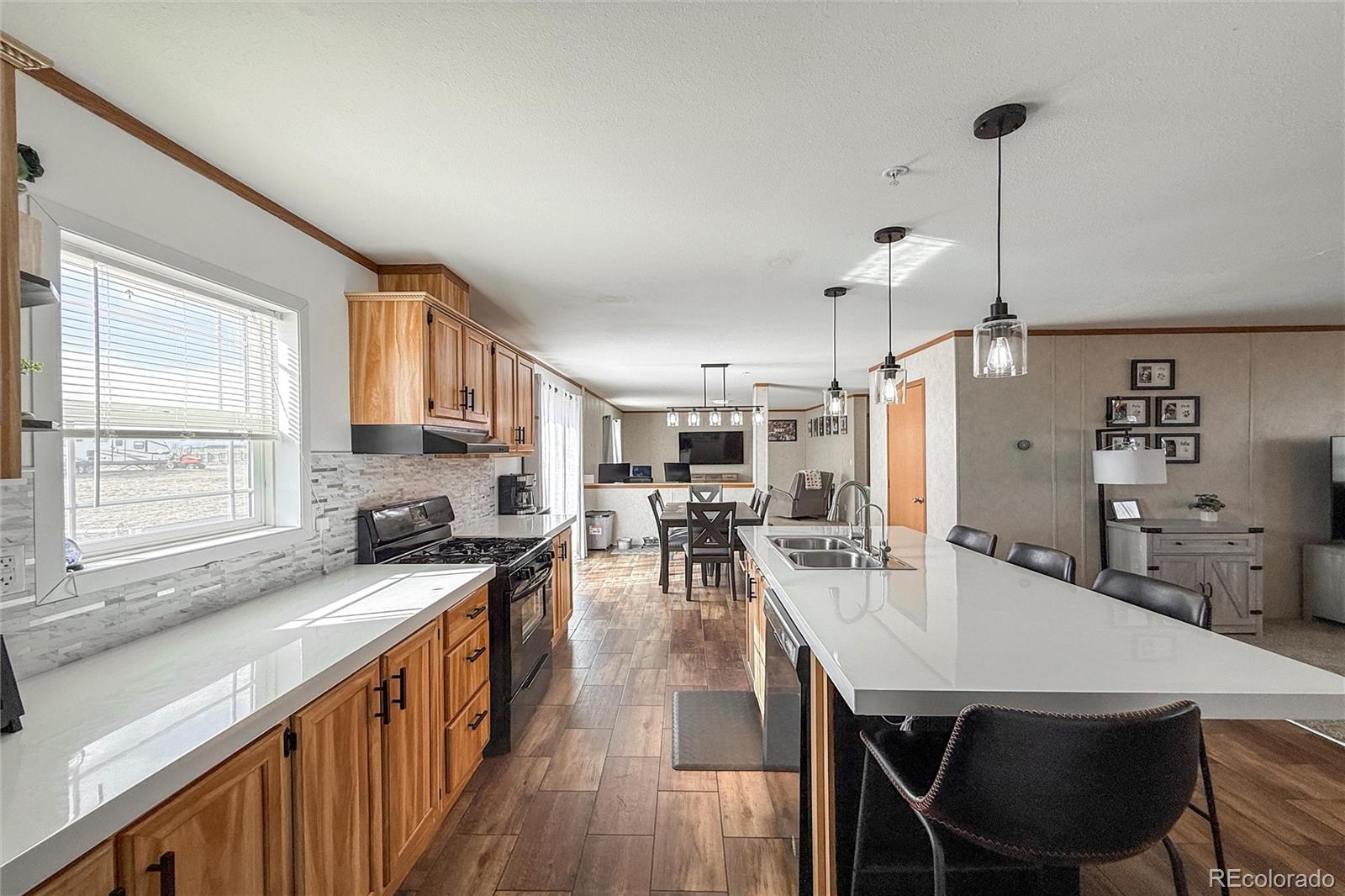 16412 Higgins Avenue Fort Lupton, CO 80621 - Photo 7 of 27 a kitchen with stainless steel appliances granite countertop a stove a sink a dining table and chairs with wooden floor