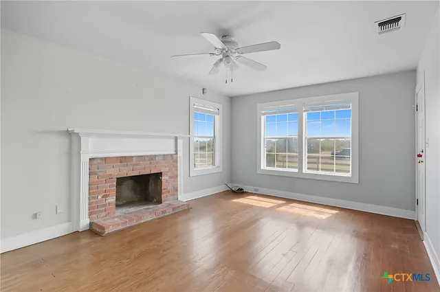 an empty room with wooden floor fireplace and windows
