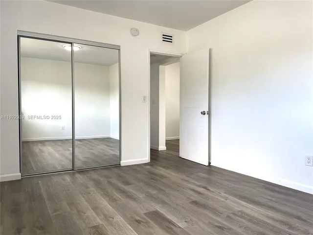 a view of an empty room with wooden floor and a bathroom