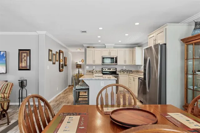 a kitchen with stainless steel appliances granite countertop a refrigerator a sink a stove a dining table and chairs with wooden floor