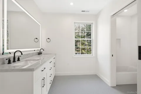 a bathroom with double vanity sink a two mirror a window and a bathtub