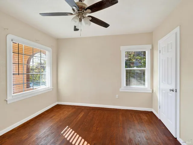 an empty room with wooden floor chandelier fan and windows
