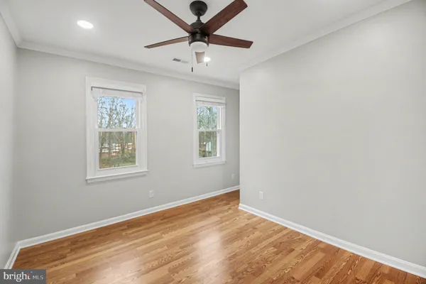 an empty room with wooden floor ceiling fan and windows