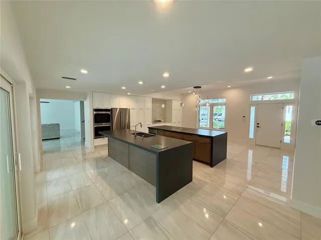 a large kitchen with stainless steel appliances a large counter top a rug a stove and a chandelier