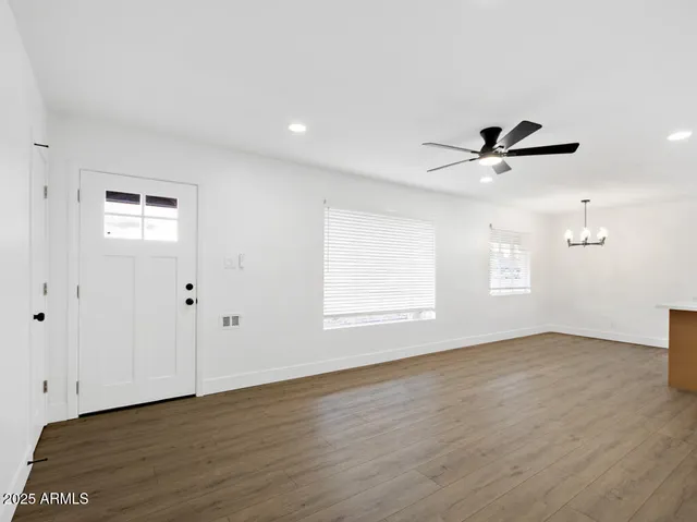 an empty room with wooden floor chandelier fan and windows