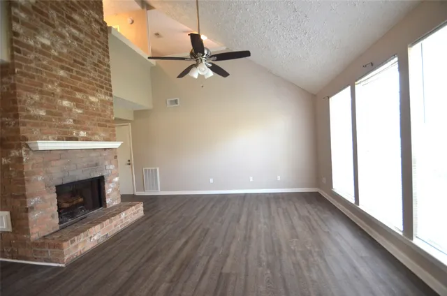 an empty room with wooden floor fireplace and windows