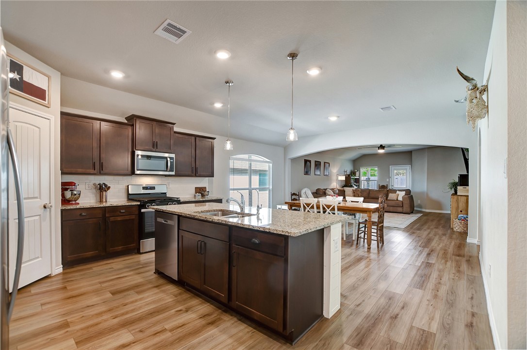 1011 Davy Street Brenham, TX 77833 - Photo 7 of 35 Spacious open-concept kitchen, dining, and living area with distinct separation. The kitchen features warm wood cabinets, granite countertops, and stainless stell appliances. It flows seamlessly into the dining and living space with ample natural light creating a warm and inviting atmosphere for time with family and friends.