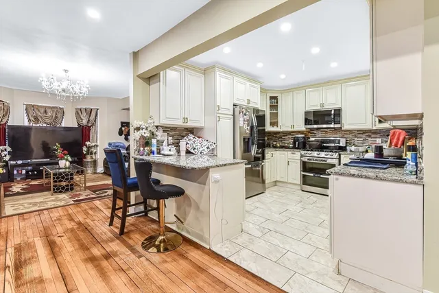 a kitchen with stainless steel appliances kitchen island granite countertop a stove top oven a sink a dining table and chairs with wooden floor