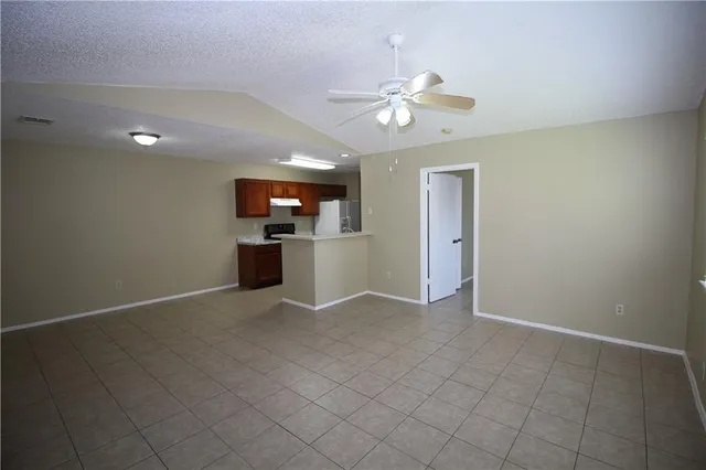 an empty room with fan and way to kitchen