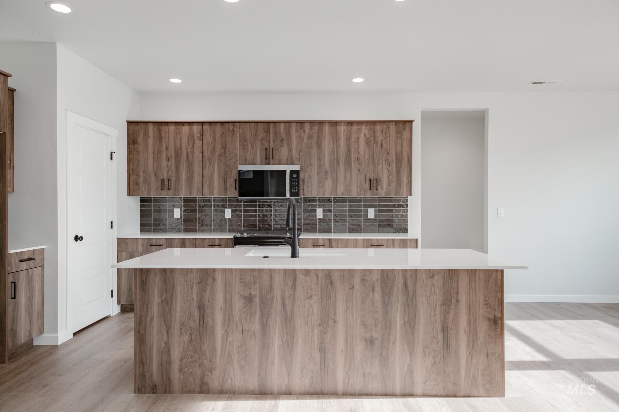 2135 South Border Way Meridian, ID 83642 - Photo 3 of 24 Kitchen with wood finish cabinets, light stone counters, an island with sink, decorative backsplash, and stainless steel microwave