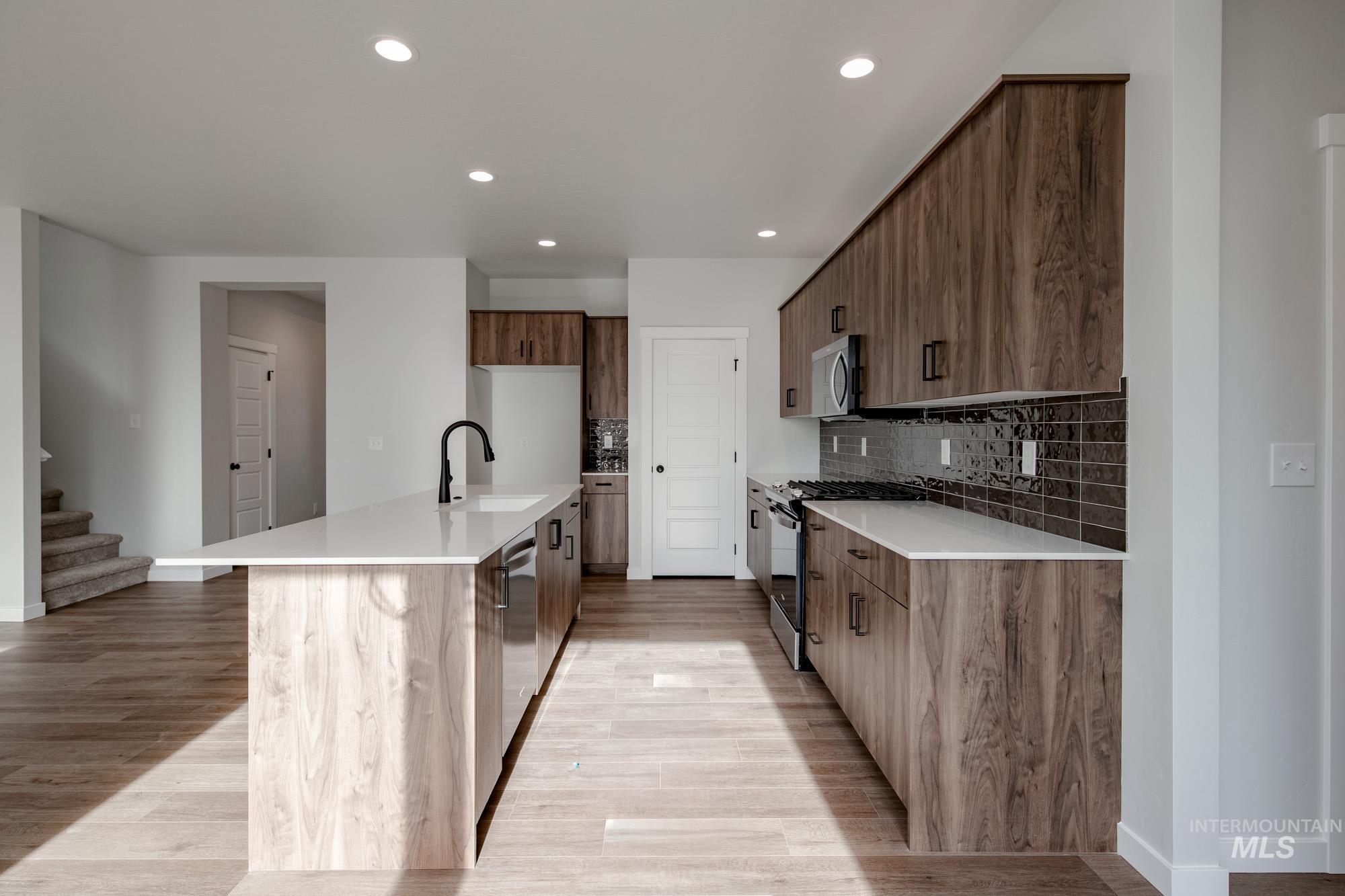 2135 South Border Way Meridian, ID 83642 - Photo 8 of 24 Kitchen featuring light stone counters, stainless steel appliances, a center island with sink, decorative backsplash, and light wood-style floors