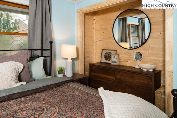 a bedroom with a bed a mirror on dresser and a large window