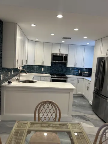 a kitchen with kitchen island granite countertop a stove a sink a refrigerator and white cabinets with wooden floor