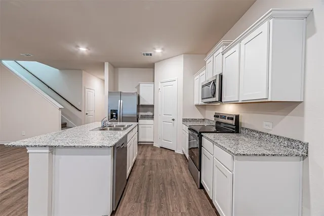 a kitchen with stainless steel appliances granite countertop a stove top oven a sink a refrigerator and white cabinets with wooden floor