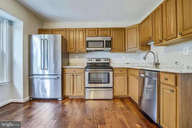a kitchen with granite countertop wooden floors stainless steel appliances and a window