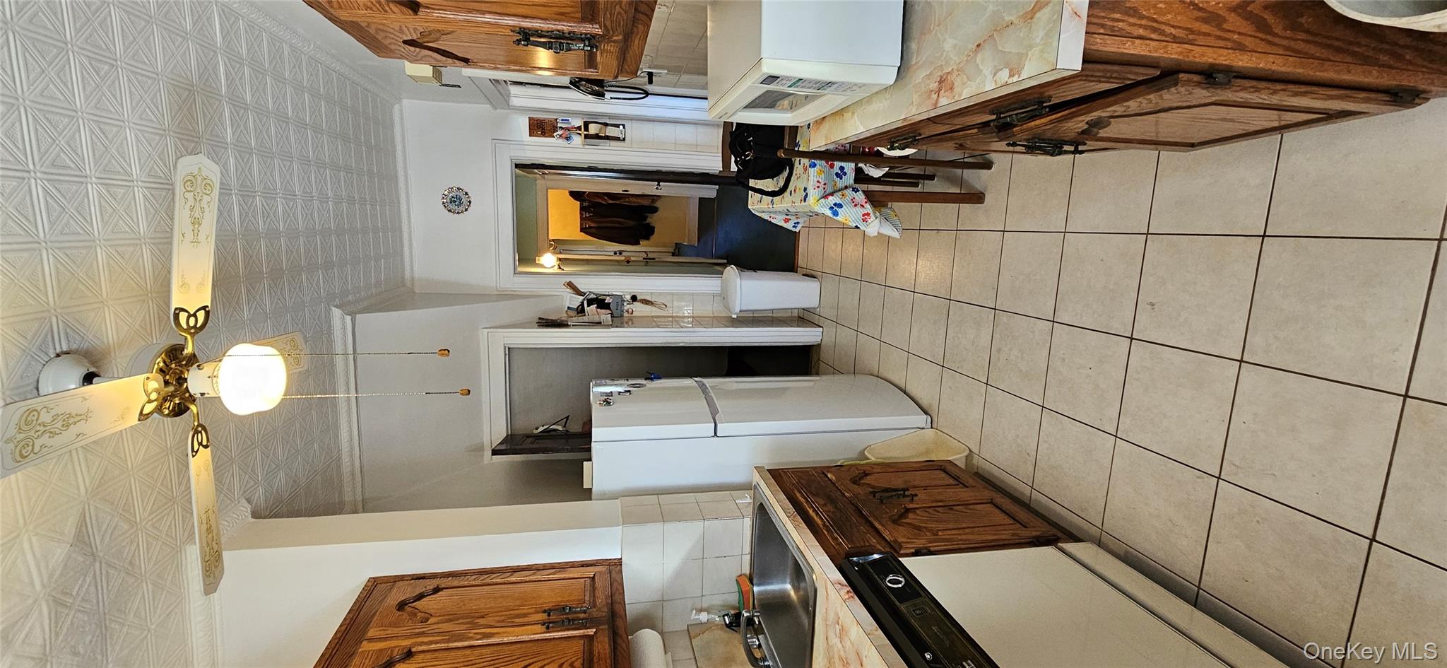 78-54 75th Street Queens, NY 11385 - Photo 9 of 31 Kitchen with brown cabinets, light countertops, decorative backsplash, dishwasher, and white refrigerator