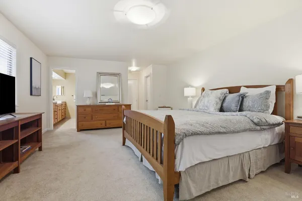 a spacious bedroom with a bed and a flat tv screen on dresser