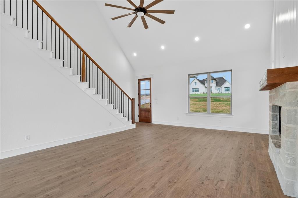 225 Kilkenny Road Poolville, TX 76487 - Photo 7 of 36 Spacious living area featuring wood-finish flooring, a stone fireplace with a wood mantel, a high vaulted ceiling with a ceiling fan, and recessed lighting