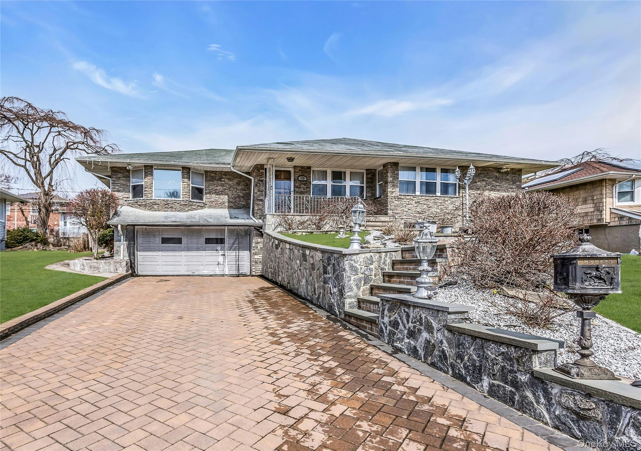 View of front of home featuring covered porch, paved driveway, a stone retaining wall, attached 1.5 garage,  front yard, and stone facade