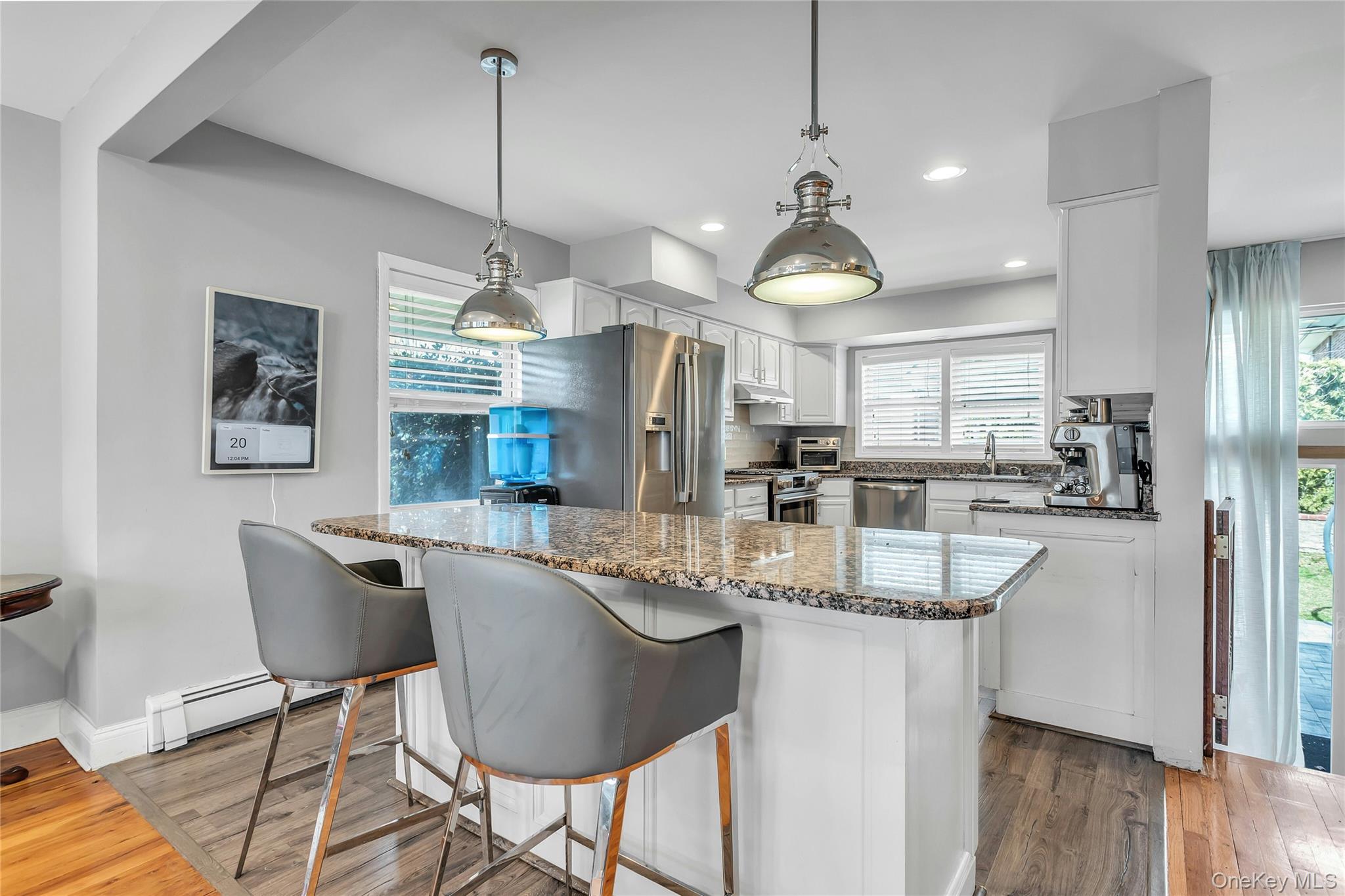 170 Old Courthouse Road Manhasset Hills, NY 11040 - Photo 12 of 35 Kitchen featuring quartz counters, white cabinets, stainless steel appliances, Center Island with seating and pendant lighting, looking out to the backyard