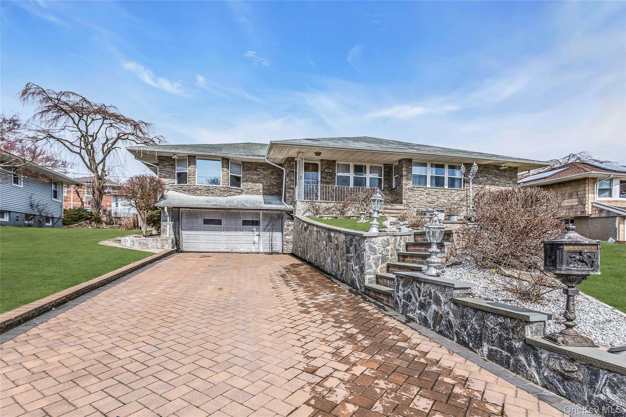 170 Old Courthouse Road Manhasset Hills, NY 11040 - Photo 34 of 35 View of front of home featuring covered porch, paved driveway, a stone retaining wall, attached 1.5 garage, front yard, and stone siding