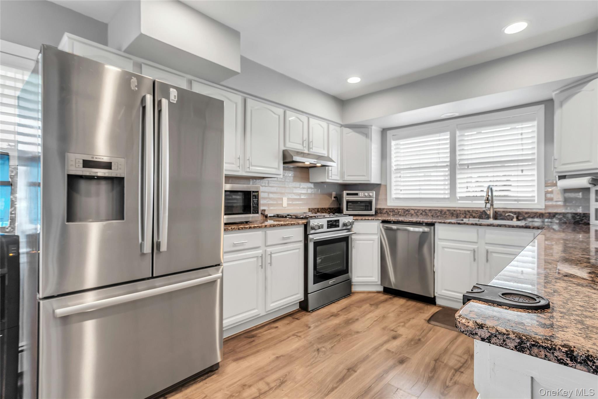 170 Old Courthouse Road Manhasset Hills, NY 11040 - Photo 9 of 35 Kitchen featuring quartz counters, white cabinets, stainless steel appliances, Center Island with seating, looking out to the backyard