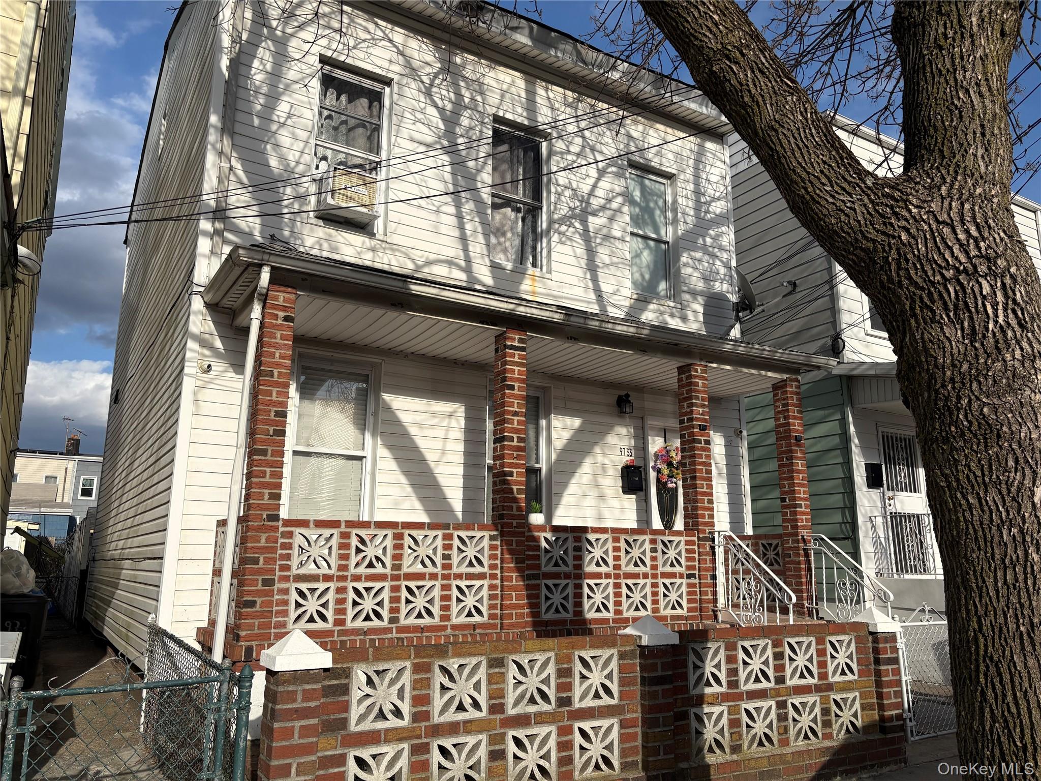 97-33 89th Street Queens, NY 11416 - Photo 1 of 12 Two-story white siding residence featuring a covered front porch supported by brick pillars