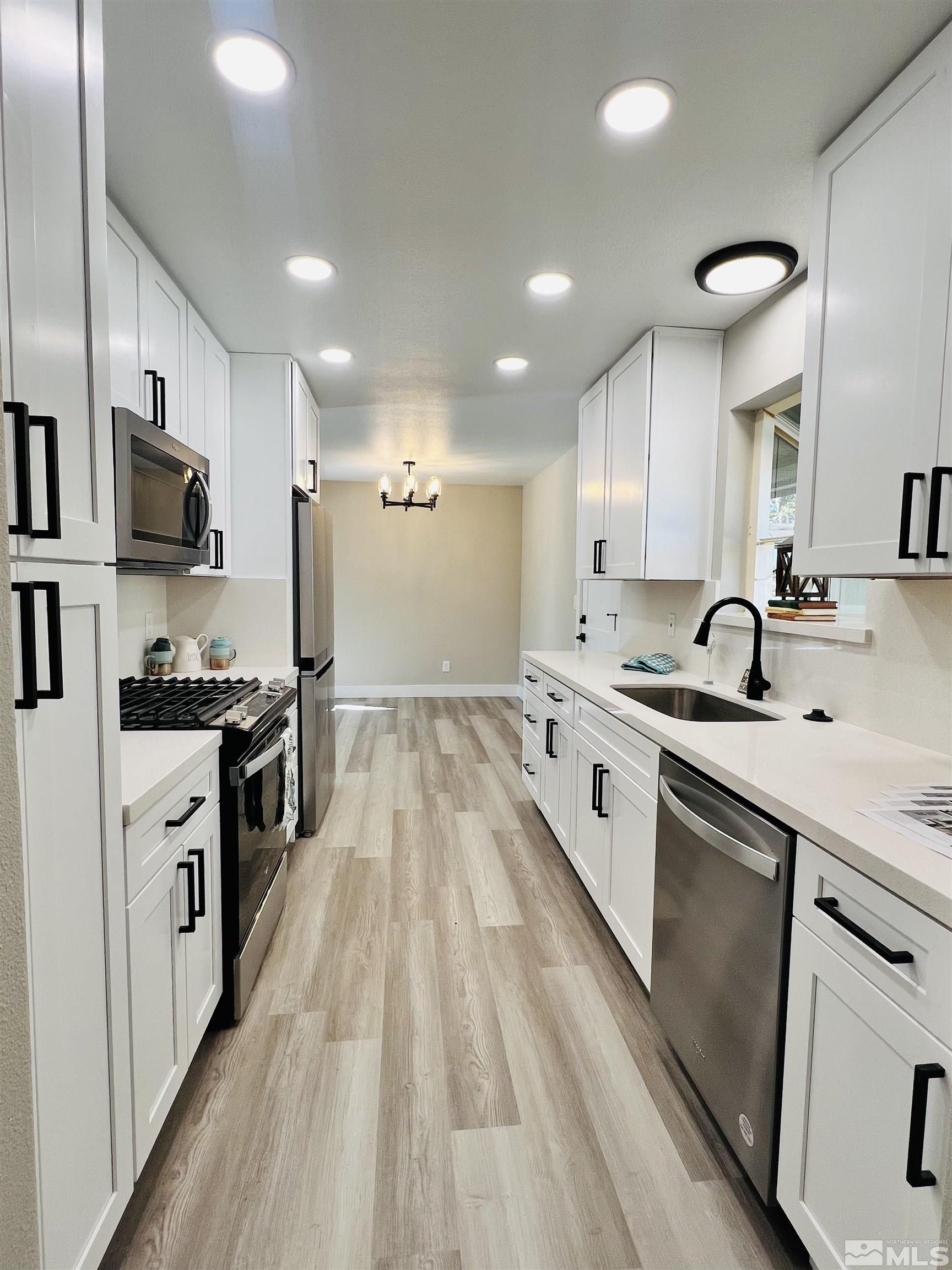a large white kitchen with stainless steel appliances granite countertop a lot of counter space and wooden floors