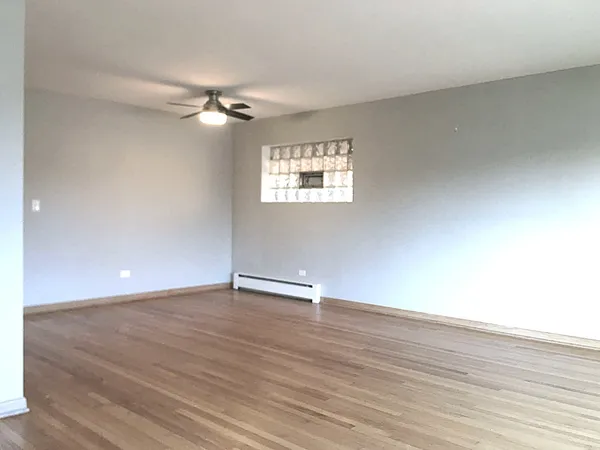 an empty room with wooden floor ceiling fan and windows