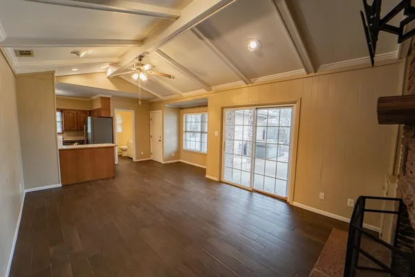 a view of an empty room with wooden floor and a kitchen