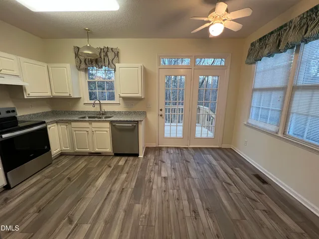 a kitchen with stainless steel appliances granite countertop a stove top oven a sink dishwasher a refrigerator and white cabinets with wooden floor