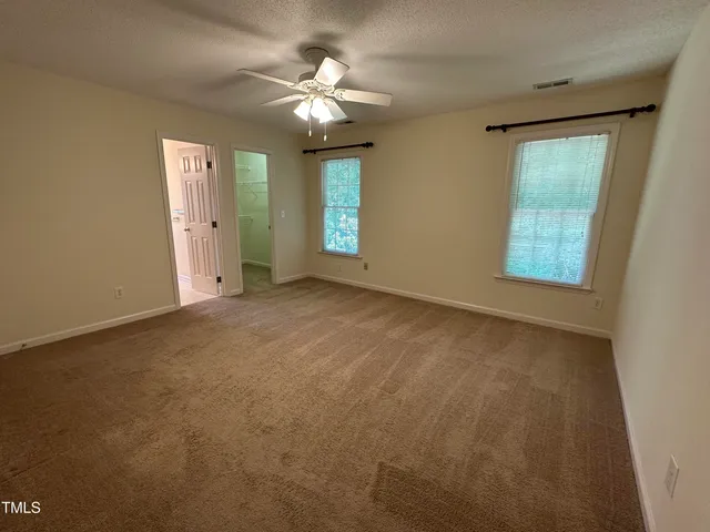 an empty room with chandelier fan and windows