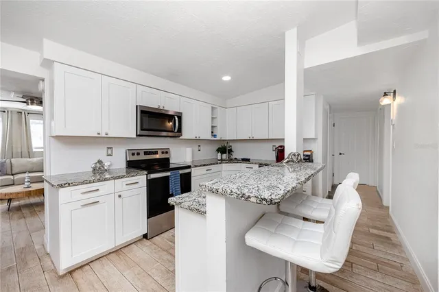 a kitchen with stainless steel appliances granite countertop a stove top oven a sink dishwasher and white cabinets with wooden floor