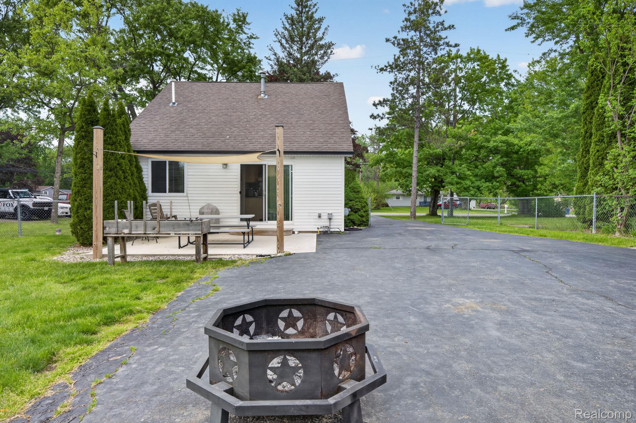 6354 Lapeer Road Burton, MI 48509 - Photo 8 of 44 Rear view of property featuring a fire pit, roof with shingles, a patio, and view of scattered trees
