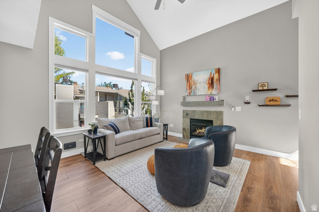 7872 Farm House Lane Midvale, UT 84047 - Photo 6 of 39 Vaulted ceiling living area featuring a prominent fireplace with a stone surround and mantel, wood-finish flooring, and expansive windows