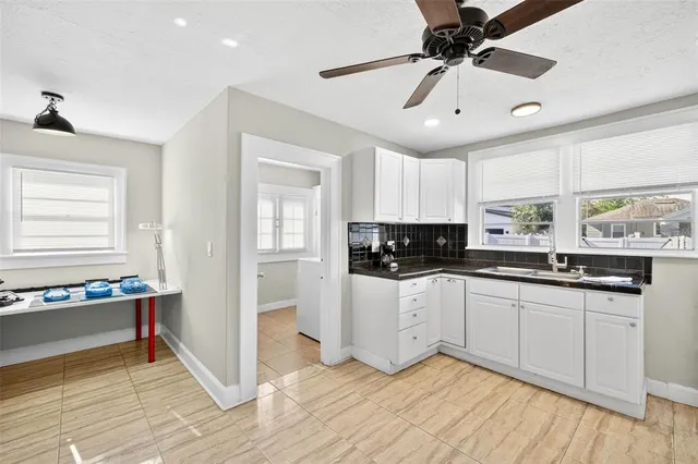 a large white kitchen with granite countertop a stove a sink and white cabinets with wooden floor next to windows