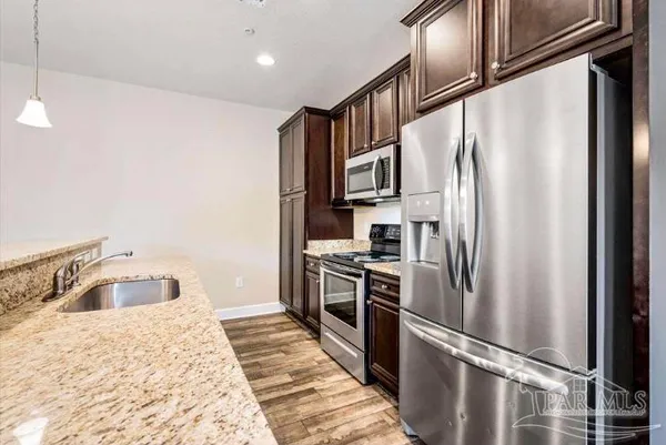a kitchen with stainless steel appliances granite countertop a refrigerator a stove and a sink with wooden floor
