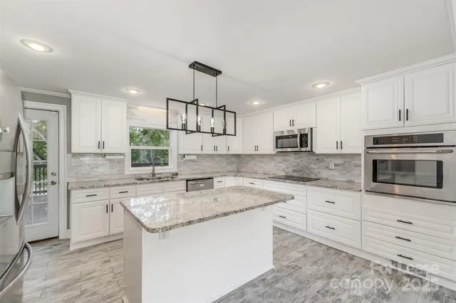 a kitchen with stainless steel appliances granite countertop a sink stove a refrigerator and a oven with white cabinets