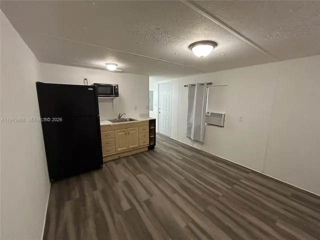a view of a refrigerator in kitchen and an empty room with wooden floor