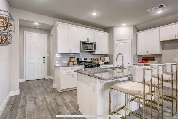 a kitchen with stainless steel appliances granite countertop a microwave a stove a sink dishwasher and a refrigerator with wooden floor