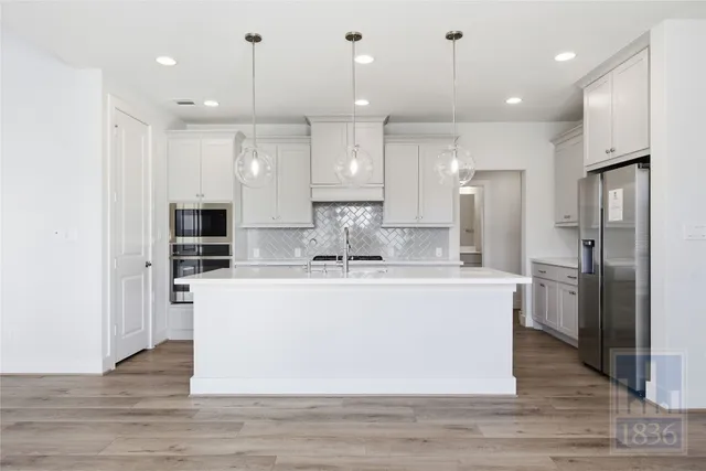 a large kitchen with stainless steel appliances granite countertop a large center island a stove a refrigerator and a view of living room