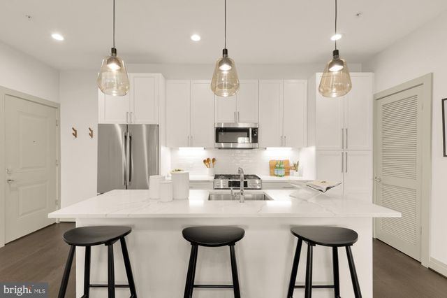 a kitchen with stainless steel appliances kitchen island granite countertop a sink a refrigerator and a wooden floor