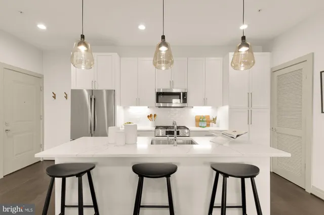 a kitchen with stainless steel appliances kitchen island granite countertop a sink a refrigerator and a wooden floor