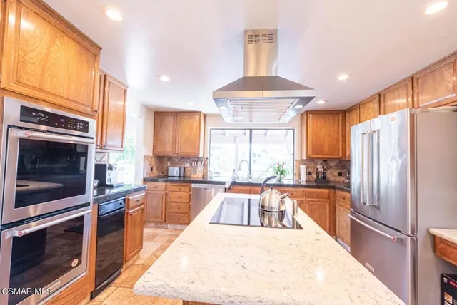 a large kitchen with stainless steel appliances kitchen island granite countertop a refrigerator a stove a sink dishwasher a dining table and chairs with wooden floor