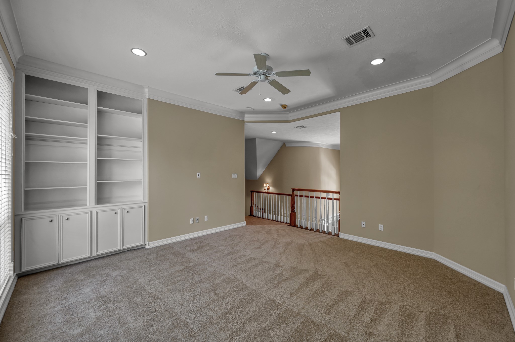 2205 Longmire Road Conroe, TX 77304 - Photo 27 of 49 This spacious room features newly carpeted flooring, built-in shelving, and a ceiling fan. Recessed lighting and a neutral color palette provide a warm atmosphere. The area overlooks the entry with wooden railing, adding an open and airy feel.