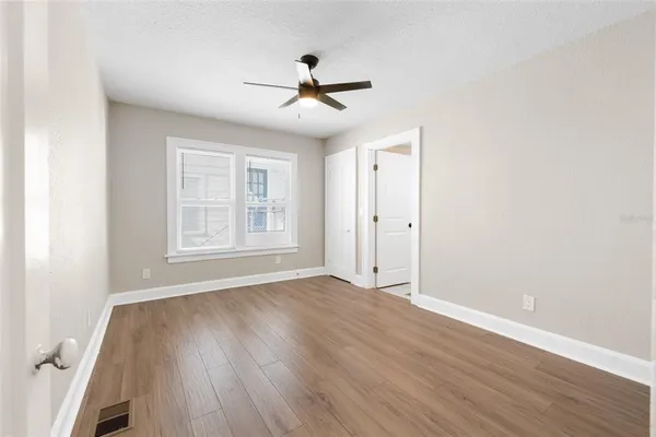 an empty room with wooden floor chandelier fan and windows