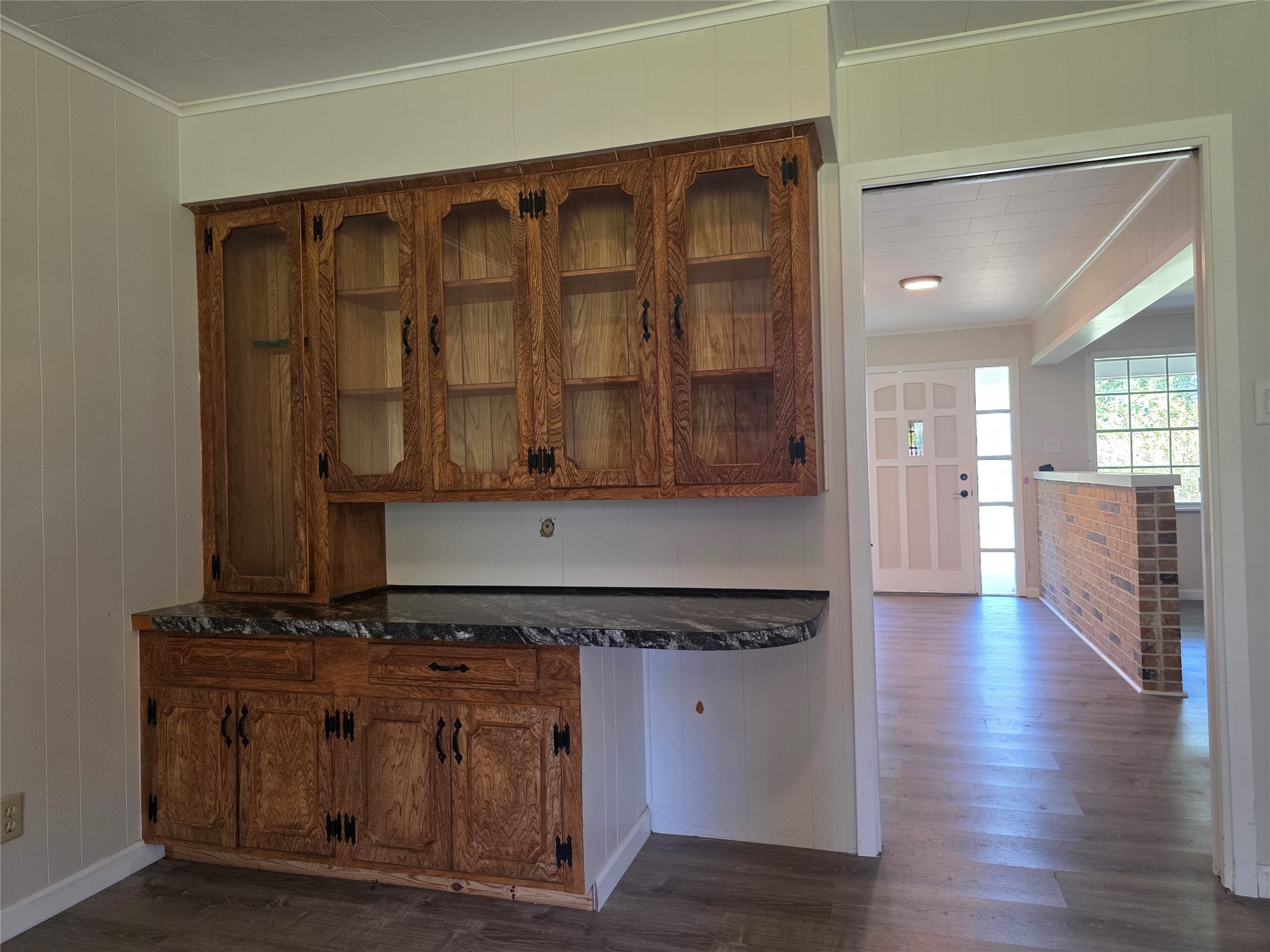 201 Verna Street Jasper, TX 75951 - Photo 11 of 24 This room features wood-paneled walls and flooring, a built-in wooden cabinet with glass doors, and a ceiling light fixture. The space opens to another room through a sliding door, offering a cozy and functional layout.