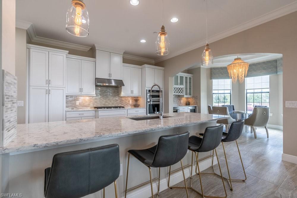 16444 Carrara Way, Unit 7301 Naples, FL 34110 - Photo 12 of 42 a kitchen with stainless steel appliances granite countertop a stove top oven a sink a dining table and chairs