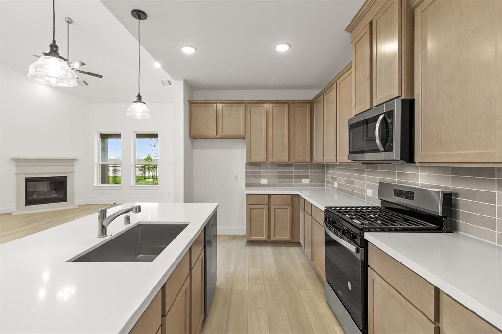8239 Red Shiner Way Fulshear, TX 77441 - Photo 1 of 25 a kitchen that has a sink a microwave oven a stove and white cabinets with wooden floor