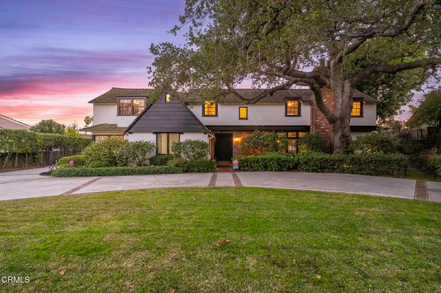 a front view of a house with a yard and a large tree